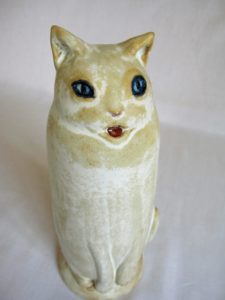 Ceramic sculpture in shades of cream of a tall cat sitting by Ellen Cooper