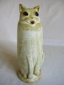 Ceramic sculpture in shades of cream of a tall cat sitting by Ellen Cooper